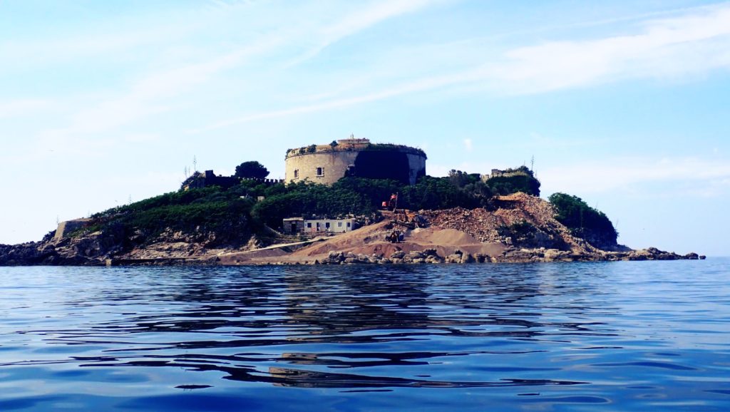 Wyspa Mamula widziana podczas rejsu. Woda i stary fort na wzniesieniu.