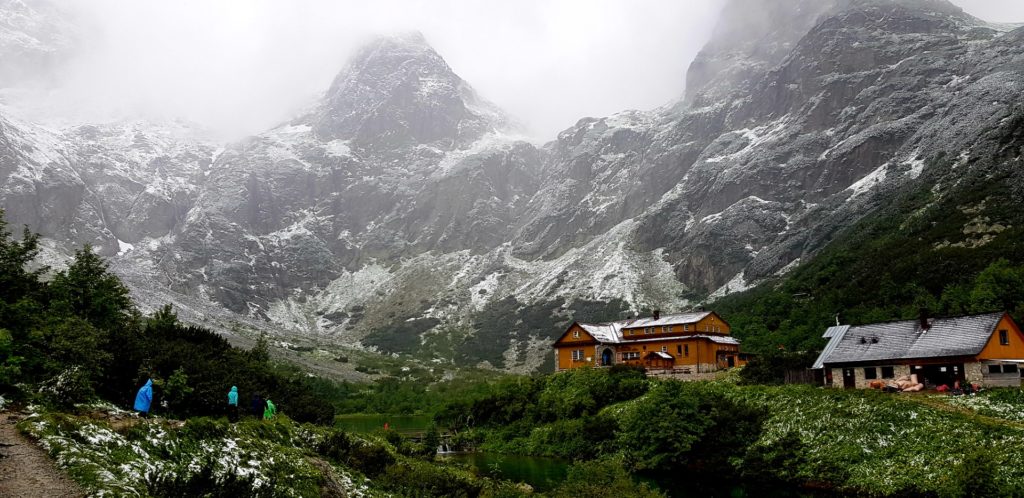 Budynki schroniska na stawem otoczone zaśnieżonymi wysokimi górami. Tatry.