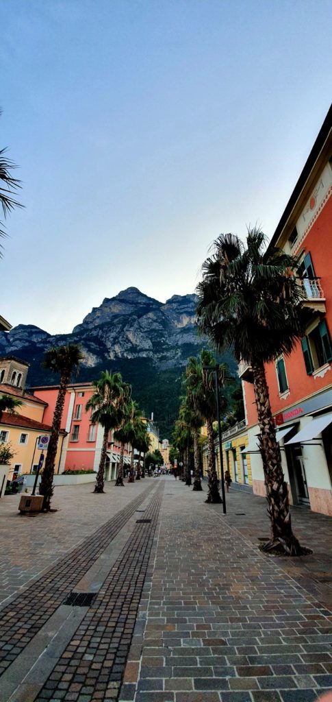 Bezludna uliczka w Riva del Garda Palny, kolorowe kamieniczki i góry w tle.