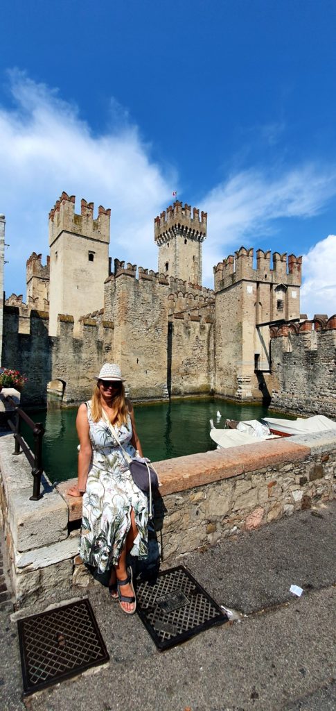 Dziewczyna w kaeluszu i letniej sukience siedząca na murku, przy zamku w Sirmione.