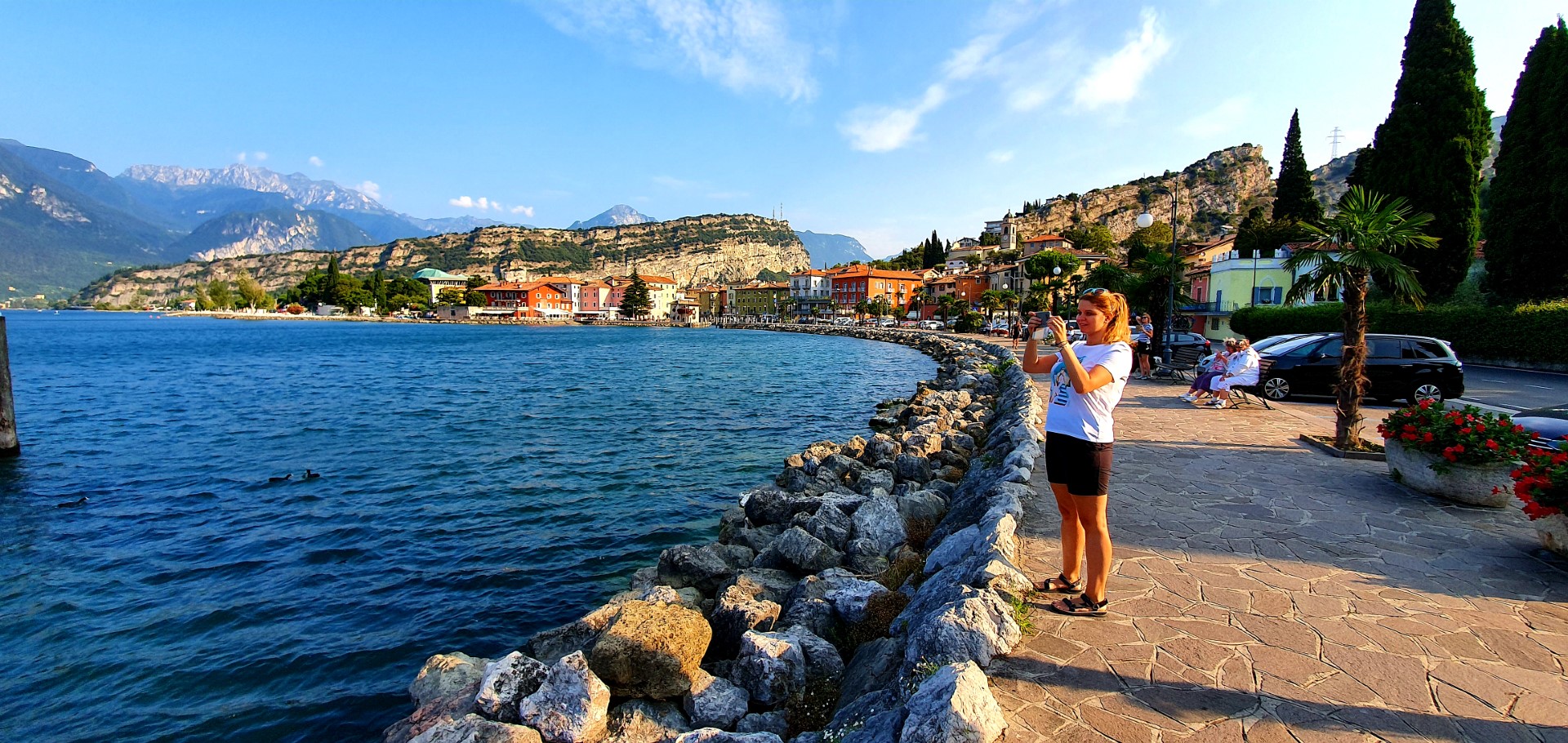 Dziewczyna robiąca zdjęcie nad brzegiem Jeziora Garda. Widok na Torbole sul Garda.