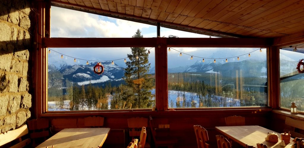 Stołu i krzesła na sali w schronisku górskim, za oknem piękny widok na góry.