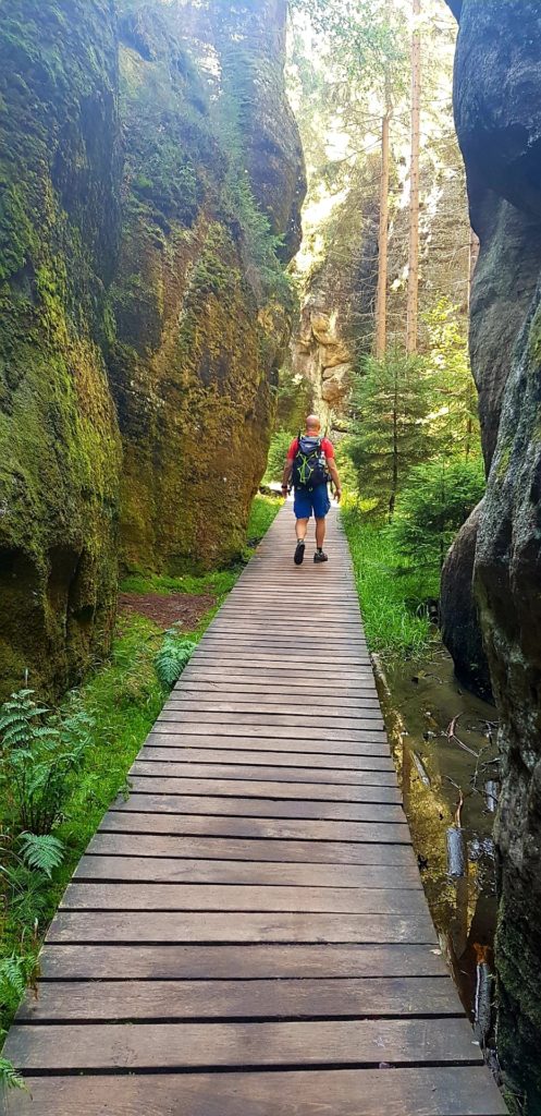 Mężczyzna z plecakiem idący drewniana ścieżką pomiędzy potężnymi skałami. Skalne miasto Adrspach, Góry Stołowe.