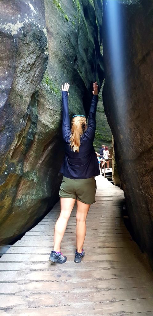 Dziewczyna w wyciągniętymi rękami przechadza się wśród skał. Skalne miasto w Górach Stołowych.