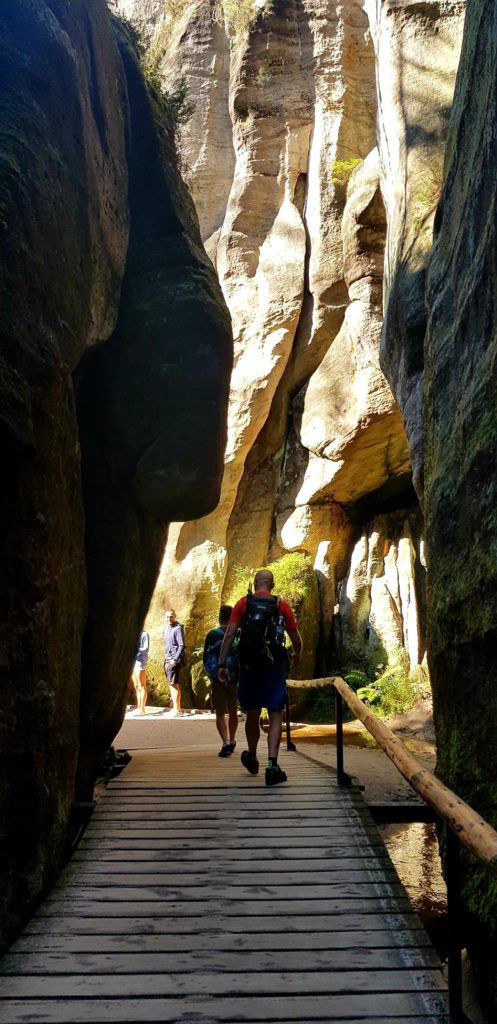 Mężczyzna z plecakiem idący drewniana ścieżką pomiędzy skałami.