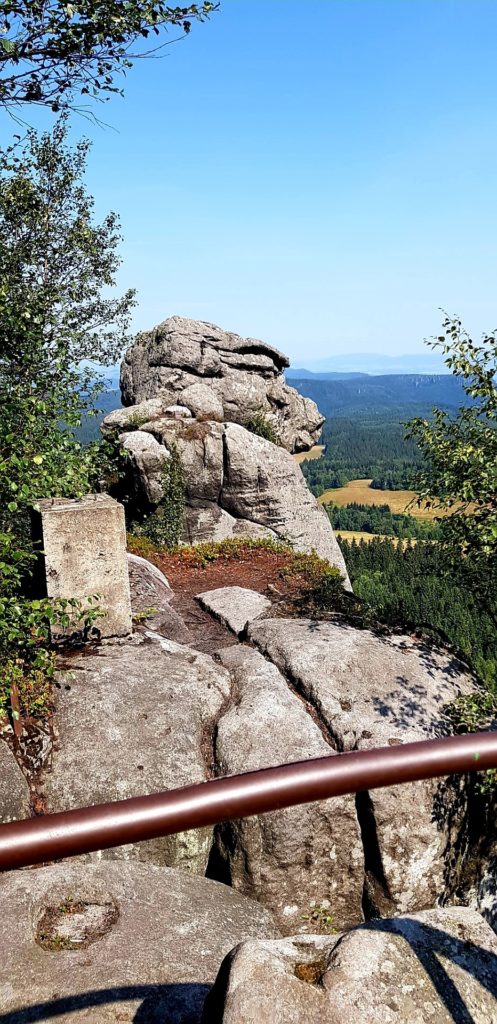 Góry Stołowe i skalna rzeźba w kształcie trolla na Szczelińcu widziana zza barierki na szlaku.