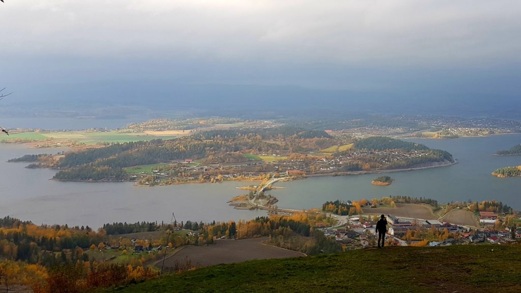 Człowiek na tle wysepek niedaleko Oslo. W dole miasteczko skąpane w jesiennych kolorach.