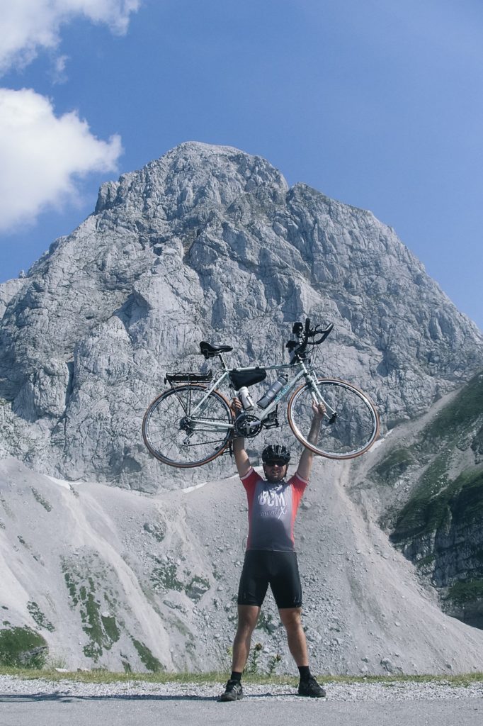 Mężczyzna trzymający w górze rower po wjeździe na Mangart.