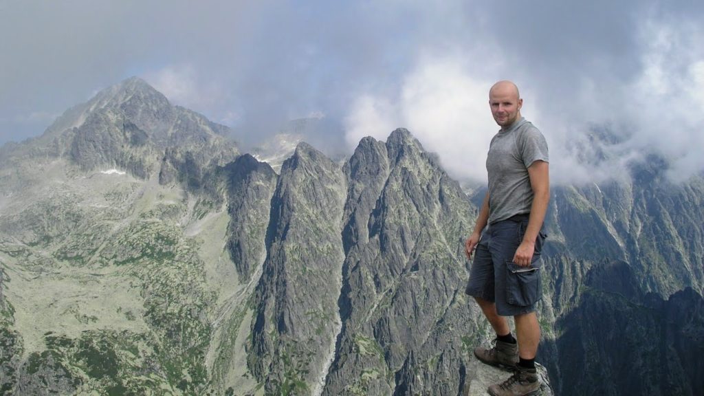 meższczyzna na gorskim szlaku stojący na kamieniu, w tle Tatry słowackie.