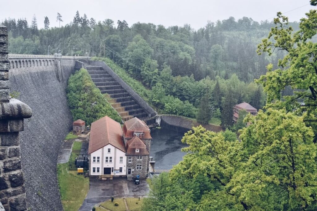 Zapora wodna widziana z góry elektrownia otoczone zielonymi drzewami.