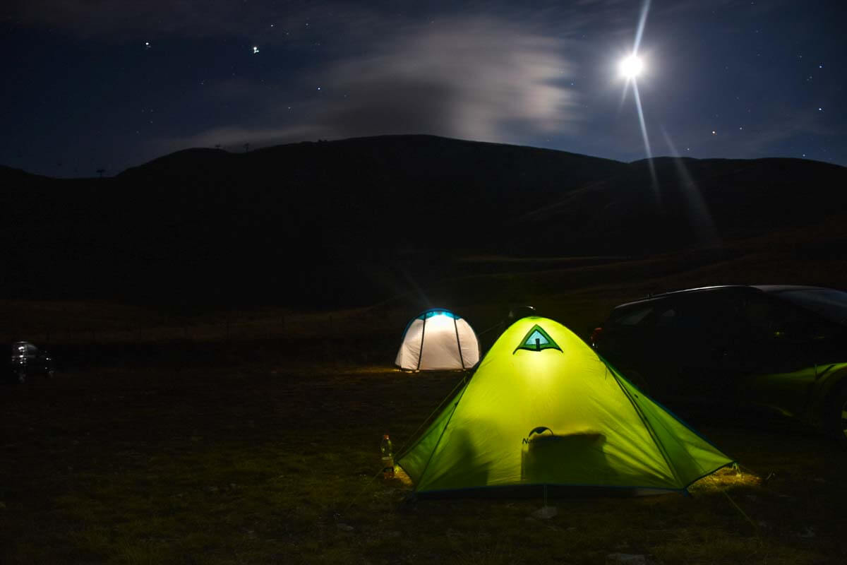 Rozświetlone namioty nocą w górach.