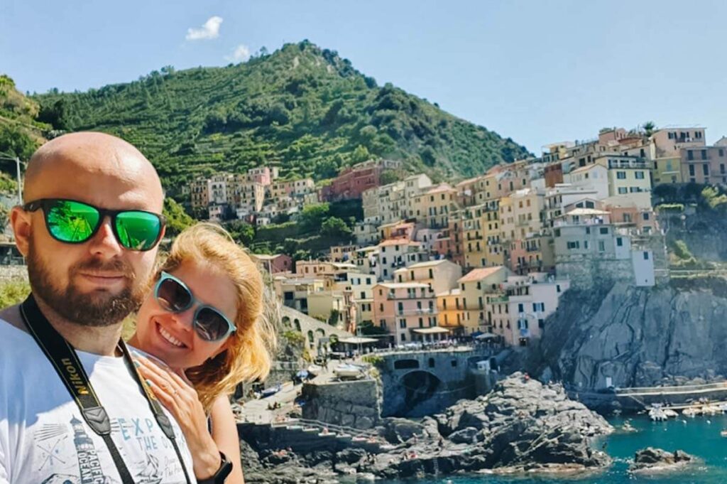 Para robiąca selfie na tle kolorowych kamienic w miasteczku Manarola.