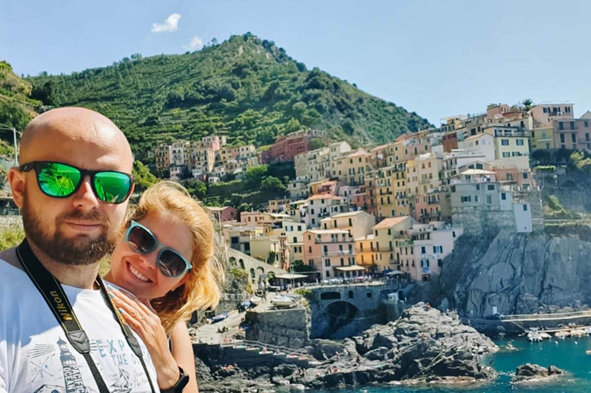 Para robiąca selfie na tle kolorowych kamienic w miasteczku Manarola.